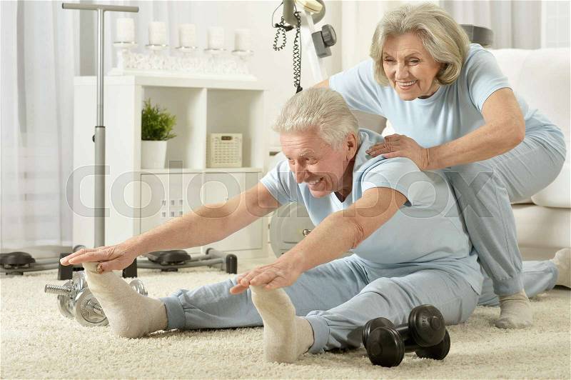 Active smiling senior couple exercising at home, stock photo