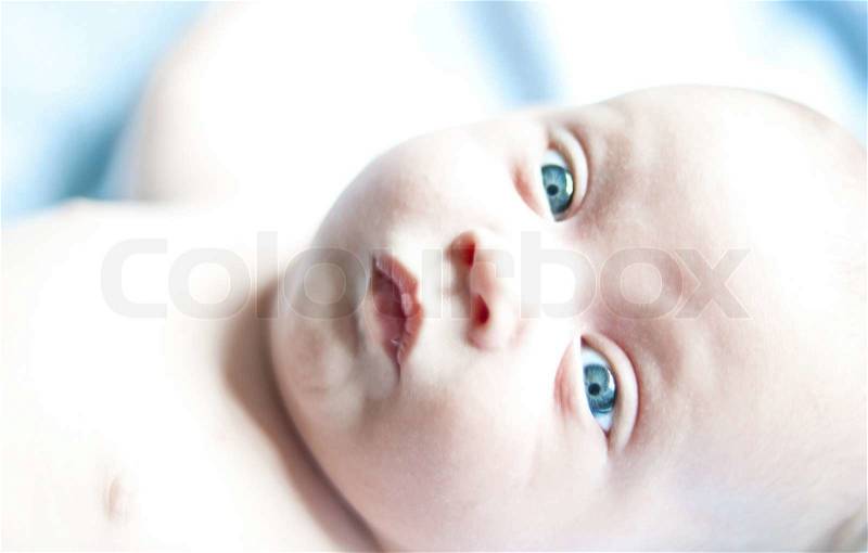 Cute newborn baby portrait close up lying on a blue sheet with eyes wide open, stock photo