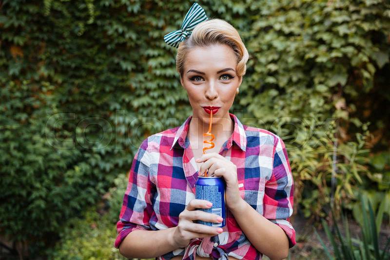 Smiling woman drinking soda with straw outdoors, stock photo