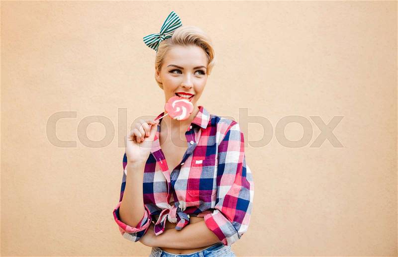 Happy cute pin up girl standing and eating colorful lollipop, stock photo