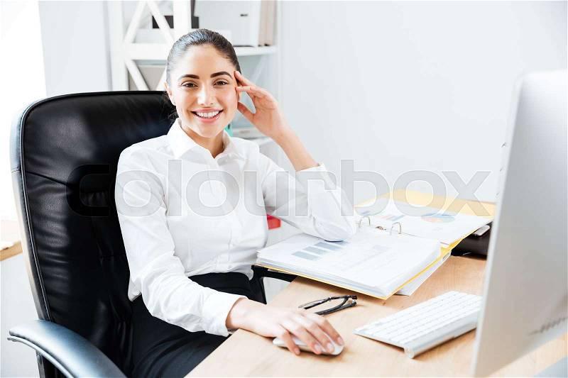 Smiling happy businesswoman sitting at the table in office, stock photo