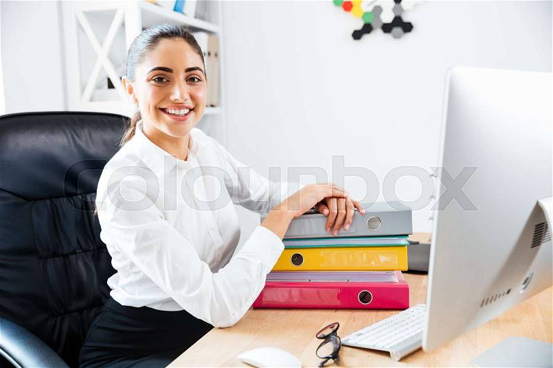 Happy cheerful businesswoman sitting at the office and looking at camera, stock photo