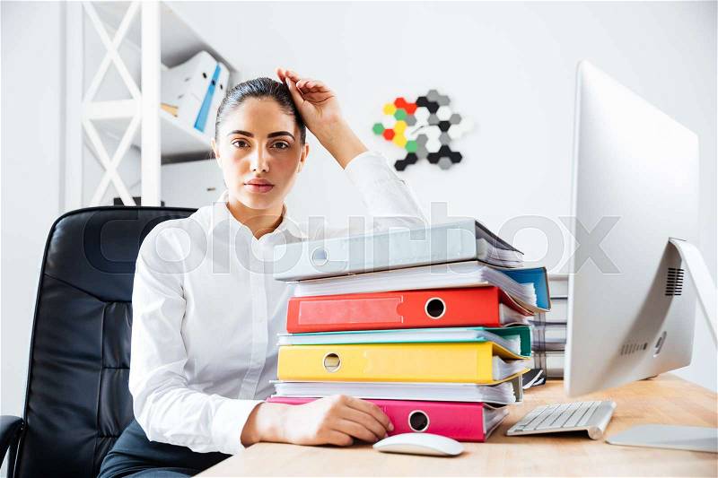 Exhausted tired businesswoman sitting at the office desk and looking at camera, stock photo