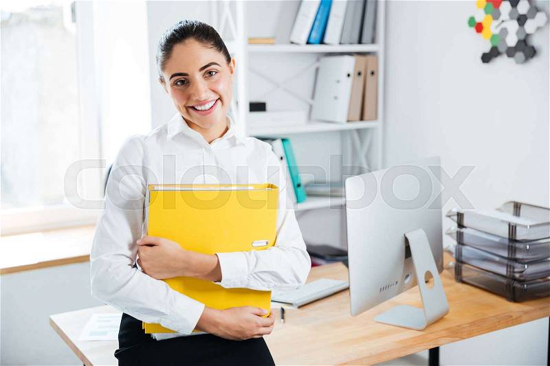 Smiling happy businesswoman sitting on the table with documents in office and looking at camera, stock photo