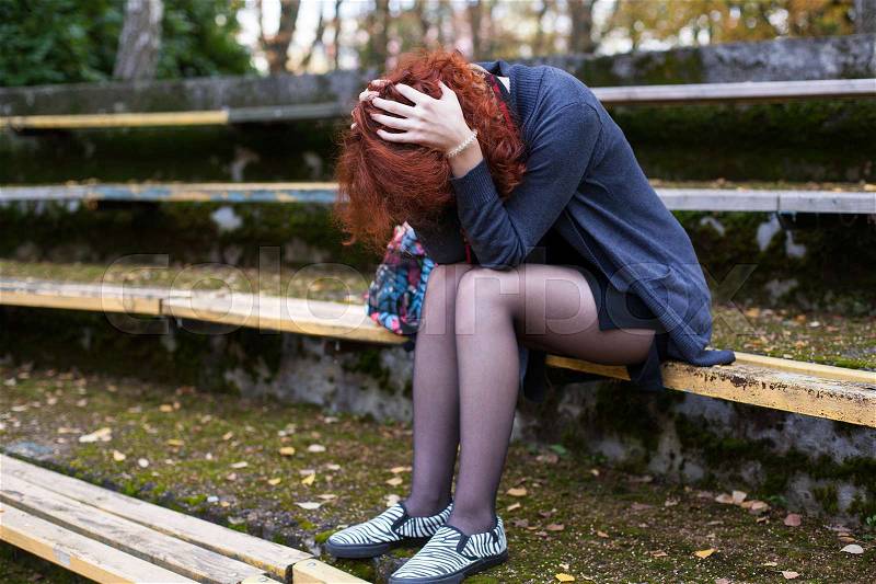 Crying woman sitting on the bench, face is hidden by the hair, head down in the hands, stock photo
