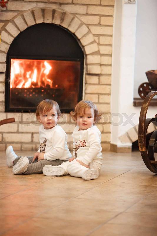 The two little girls sitting at home against the fireplace, stock photo