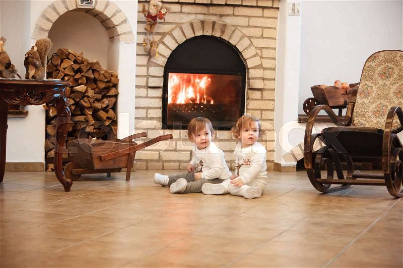 The two little girls sitting at home against the fireplace, stock photo