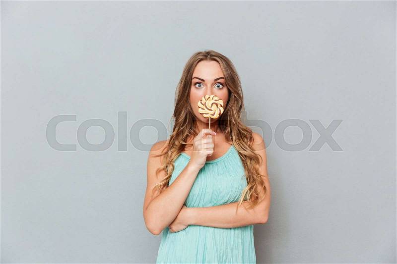 Funny cute young woman covered her mouth with lollipop, stock photo