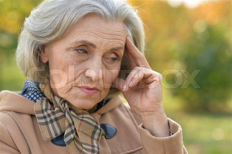 Portrait of a sad elderly woman in autumn park, stock photo