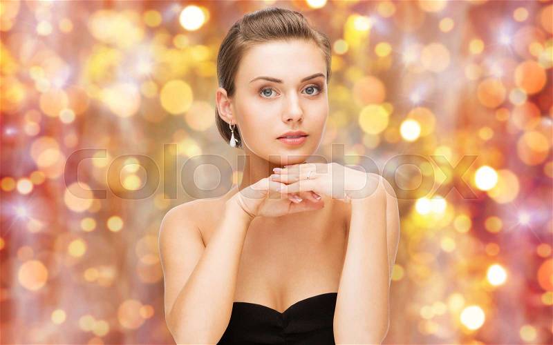 Beauty, luxury, people, holidays and jewelry concept - beautiful woman with diamond ring and earrings over lights background, stock photo