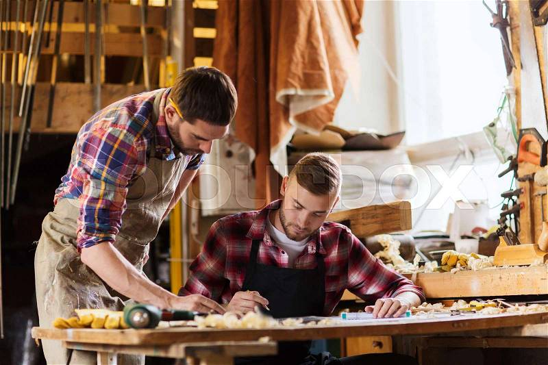 Profession, carpentry, woodwork and people concept - two carpenters with ruler and blueprint at workshop, stock photo