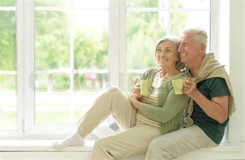 Happy Senior couple drinking tea sitting on windowsill at home, stock photo