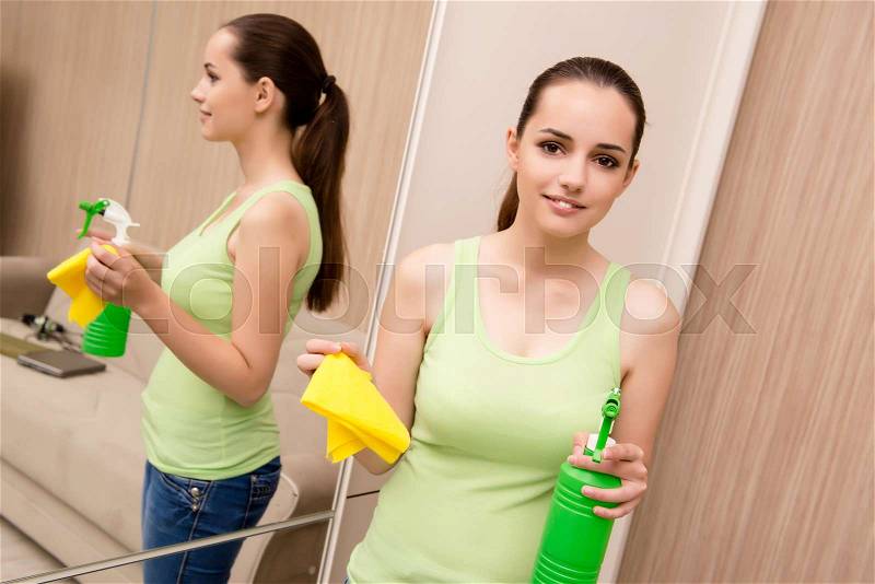 Young woman cleaning mirror at home, stock photo