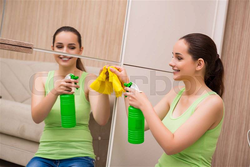 Young woman cleaning mirror at home, stock photo