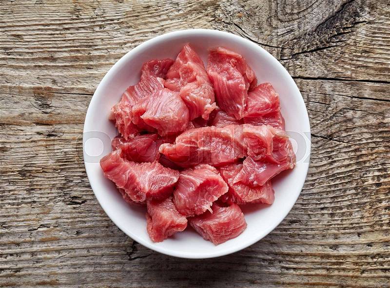 White bowl of raw diced beef meat on wooden table, top view, stock photo