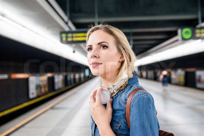 Beautiful young woman in denim shirt with earphones, standing at the underground platform, waiting, stock photo