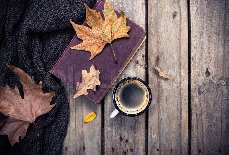 Old book, knitted sweater with autumn leaves and coffee mug on vintage wooden board background, stock photo