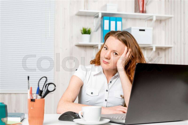 Young receptionist sitting behind a desk in the office, stock photo