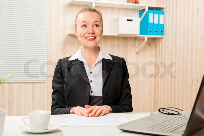 Pretty cheerful woman in a suit behind a computer, stock photo
