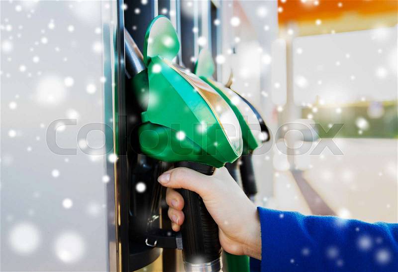 Winter, fuel, oil, tank and transport concept - close up of hand holding gasoline hose at gas station over snow, stock photo