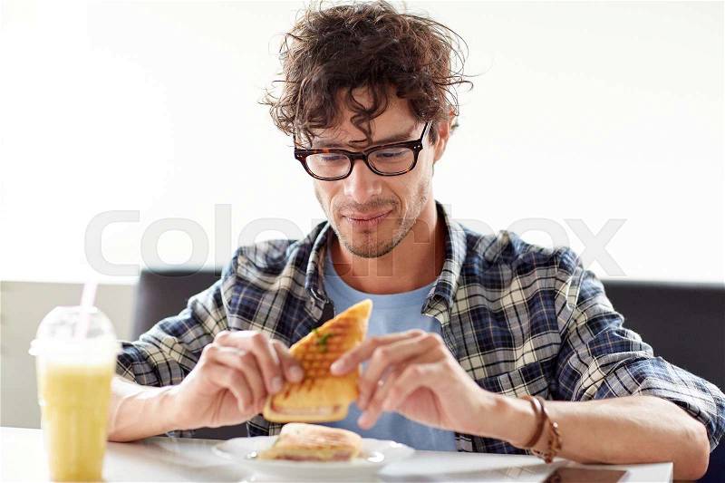 Leisure, food, eating and people concept - happy man eating sandwich at cafe for lunch, stock photo