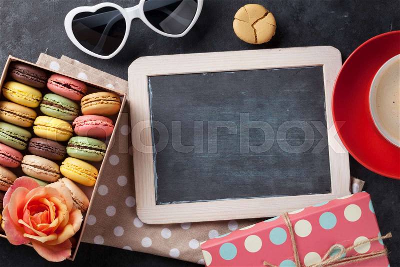 Colorful macaroons, coffee and blackboard. Sweet macarons in gift box on stone table. Top view with copy space, stock photo