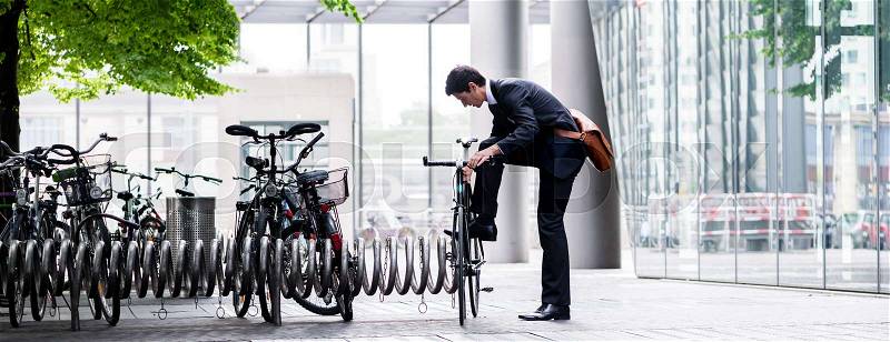 Businessman parking his bicycle in town at a bicycle rack after commuting to work in a concept of eco-friendly transport and healthy active lifestyle, panoramic banner view, stock photo