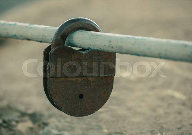 Shut up, old, worn, rusty, shabby padlock hanging on painted, worn, cut, pipe outdoors, stock photo