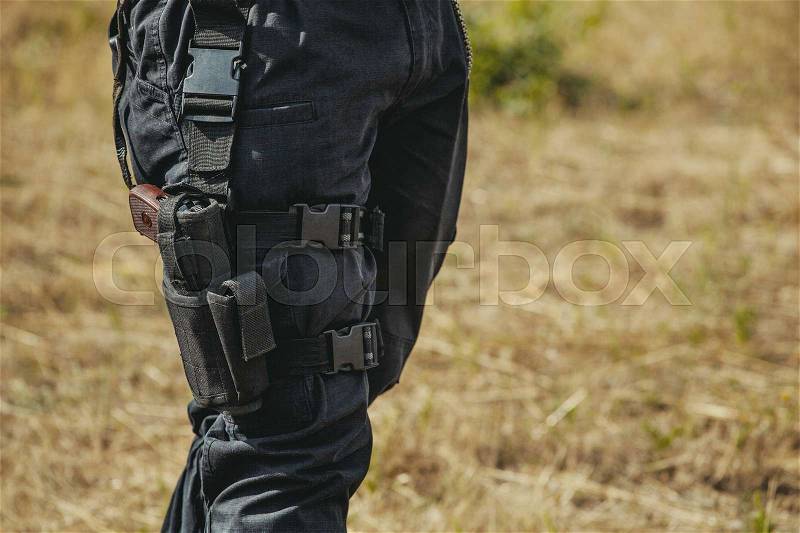 The gun hidden in a holster hanging on a soldier\'s leg, stock photo