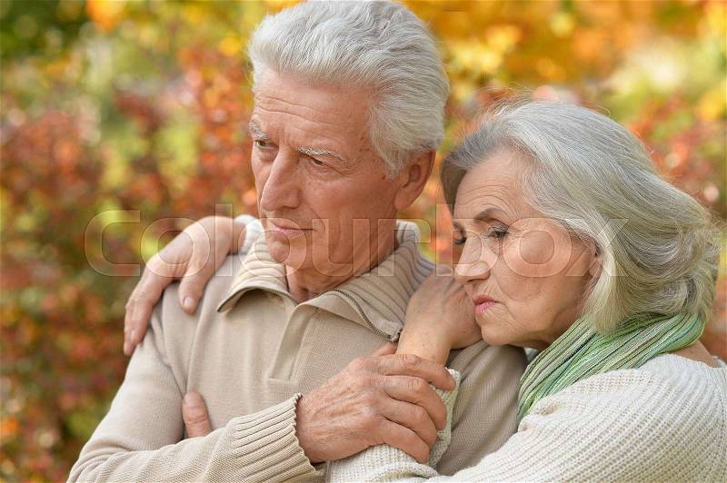 Portrait of a sad elderly couple standing embracing outdoors, stock photo