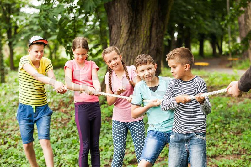 Group of happy smiling kids playing tug-of-war with rope in green park,, stock photo