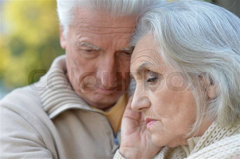 Portrait of a sad elderly couple standing embracing outdoors, stock photo