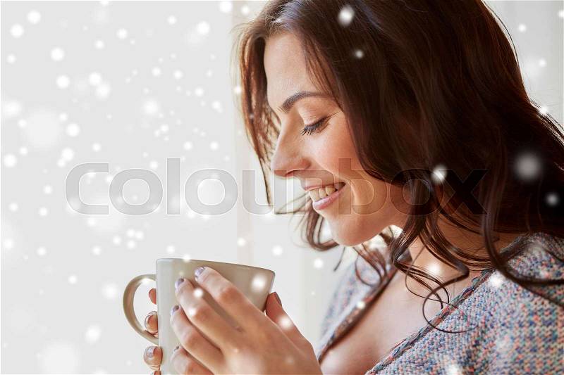 People, drinks, christmas and winter concept - close up of happy young woman with cup of tea or coffee at home over snow, stock photo