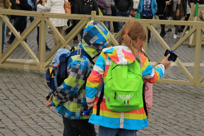 The boy and the two girls in striking raincoats are looking to the selfie they have made in one of the streets in the city Rome in Italy in the summer, stock photo