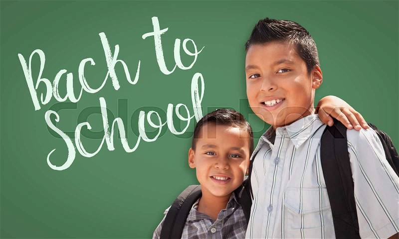 Cute Hispanic Boys Wearing Backpacks In Front of Back To School Written On Chalk Board, stock photo