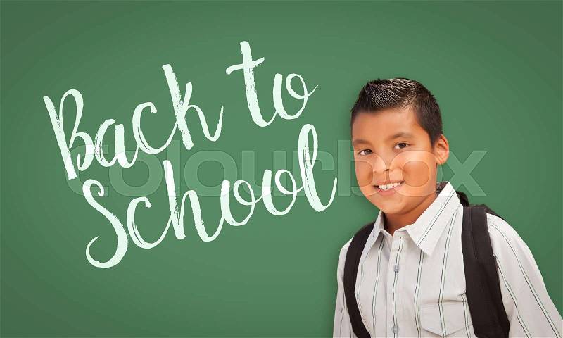 Cute Hispanic Boy Wearing A Backpack In Front of Chalk Board with Back To School Written On it, stock photo