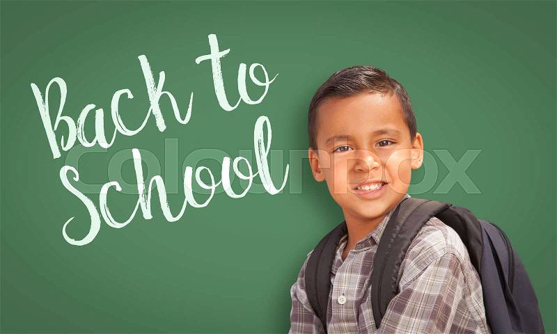 Cute Hispanic Boy Wearing A Backpack In Front of Chalk Board with Back To School Written On it, stock photo