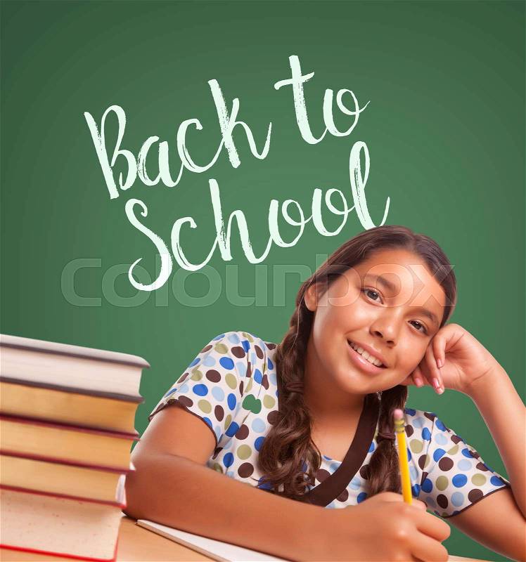 Cute Smiling Hispanic Girl Studying In Front of Back To School Written on Chalk Board, stock photo