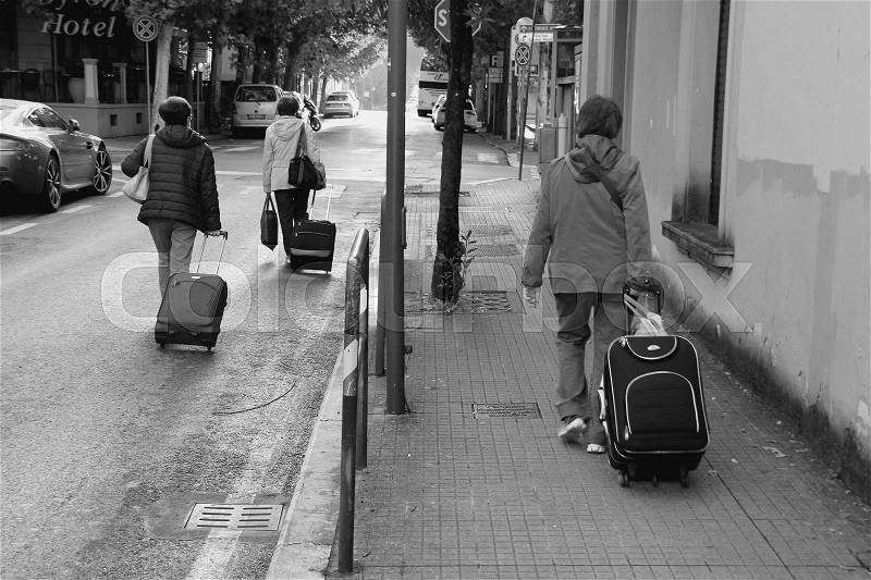 The ladies with the trolley suitcases are walking on the path or at the street in the city Montecatini in Italy at sunrise in the summer in black and white, stock photo