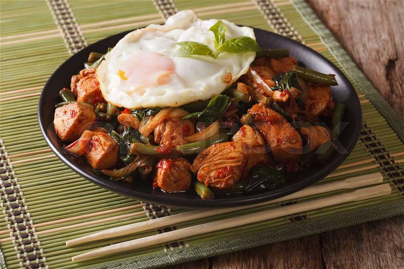 Spicy Stir-Fry Chicken with basil, green beans and a fried egg on a plate close-up horizontal , stock photo