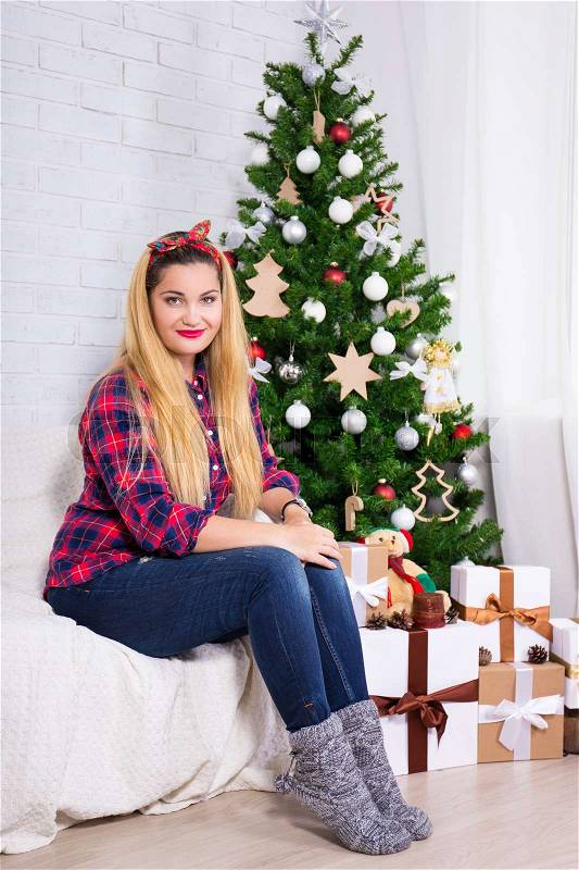 Portrait of young beautiful woman in decorated room with Christmas tree, stock photo