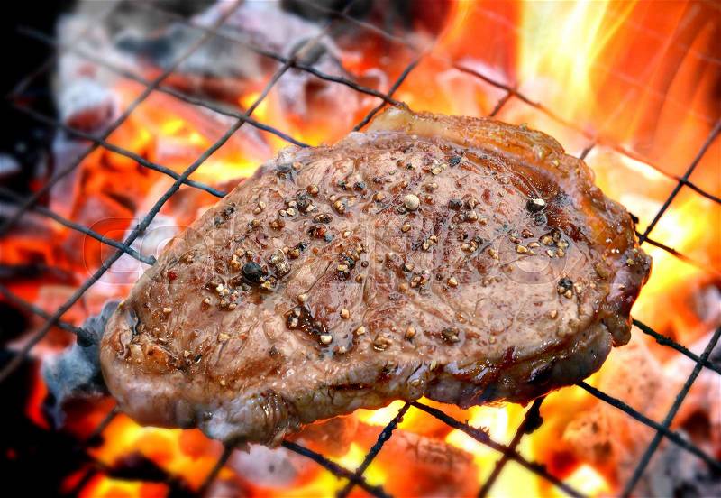 Grilling pepper steaks on flaming in outdoor lighting, stock photo