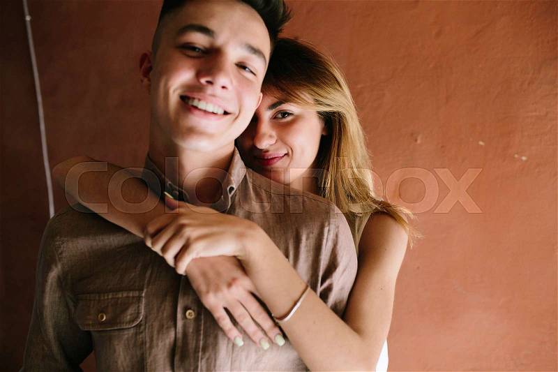 Girl hugging guy from behind on a background of an orange wall, stock photo