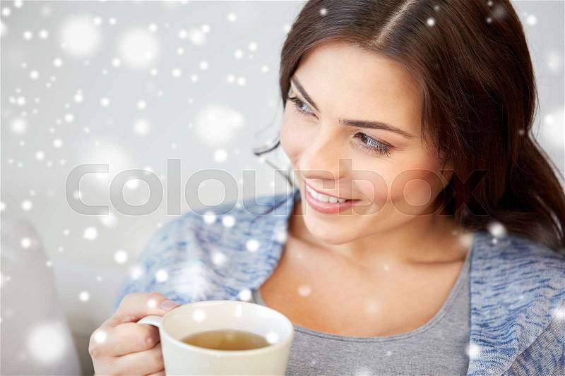 People, drinks, christmas and winter concept - happy young woman with cup of tea at home over snow, stock photo