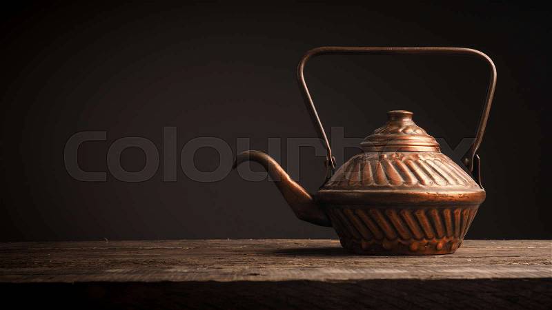 Old copper tea pot on a rustic wooden table with space for text, stock photo