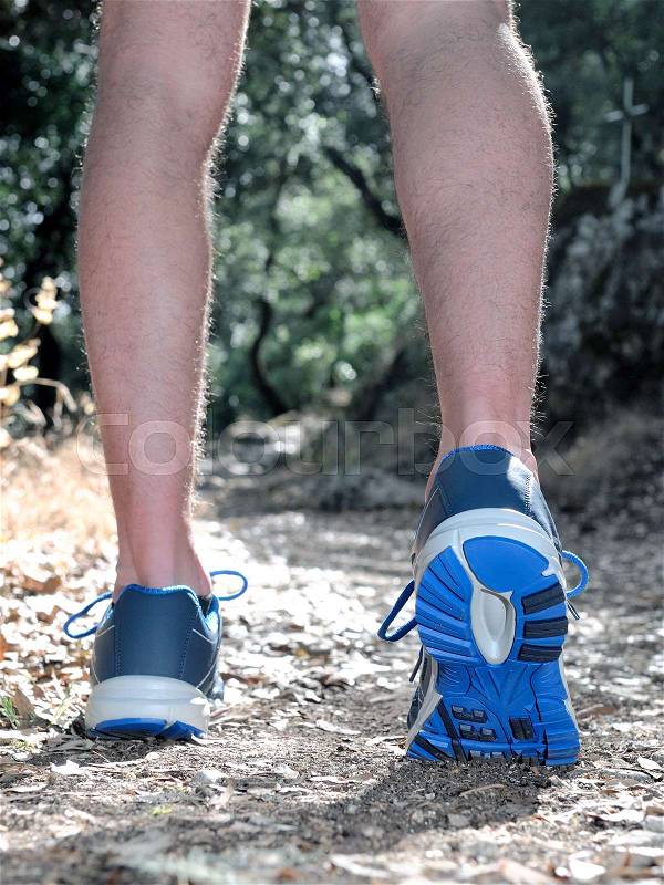 Running shoes close-up of a young man doing physical exercise walking between trees on a mountain path, stock photo