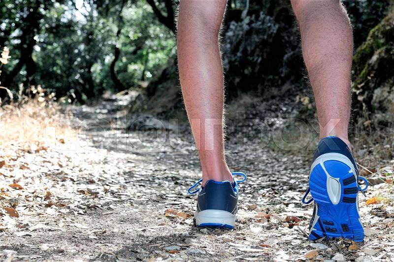 Running shoes close-up of a young man doing physical exercise walking between trees on a mountain path, stock photo