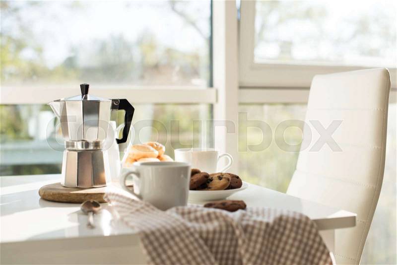 Early morning french home breakfast, coffee and cookies on the table near window in bright sunlight, white interior, stock photo