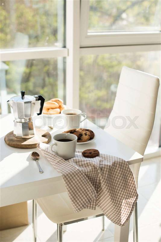 Early morning french home breakfast, coffee and cookies on the table near window in bright sunlight, white interior, stock photo
