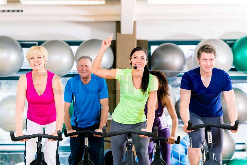 Group of men and women spinning on fitness bikes in gym, diversity people, old, young, black and white, stock photo